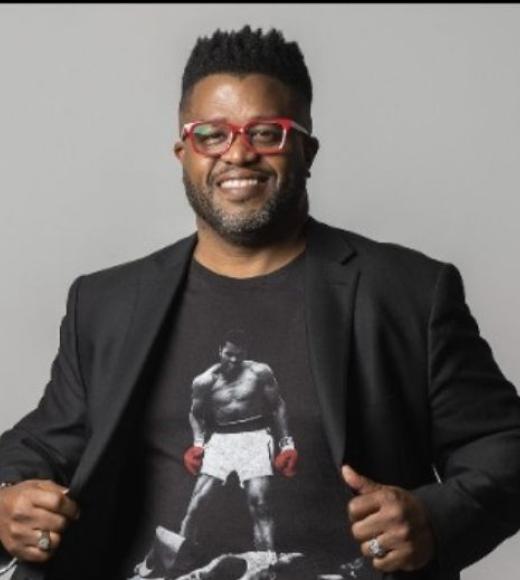 Smiling man in red glasses and black blazer revealing t-shirt with vintage boxing photograph.