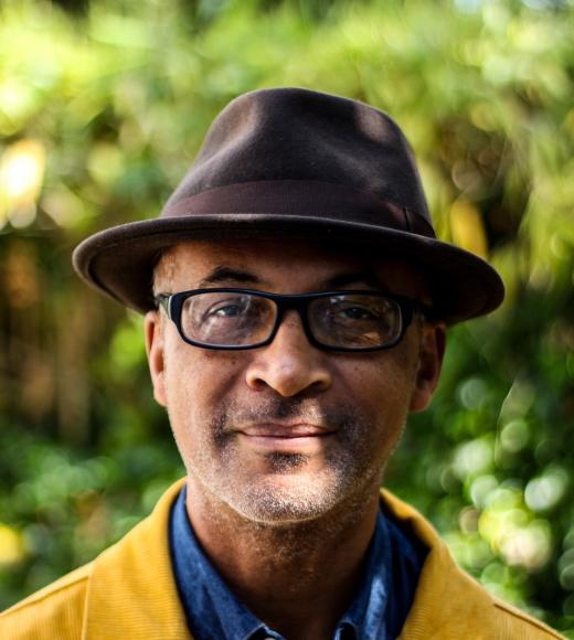 photo of Colin Grant, wearing a hat and a yellow coat, standing in front of a background of trees